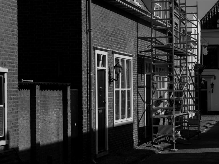 Straat met bakstenen rijwoningen; tegen een van de gevels staat een stelling.
