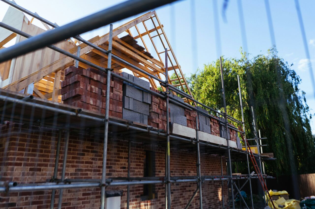 Nieuwbouwwoning in rode gevelsteen achter een stelling, met de houten dakspanten al geplaatst.