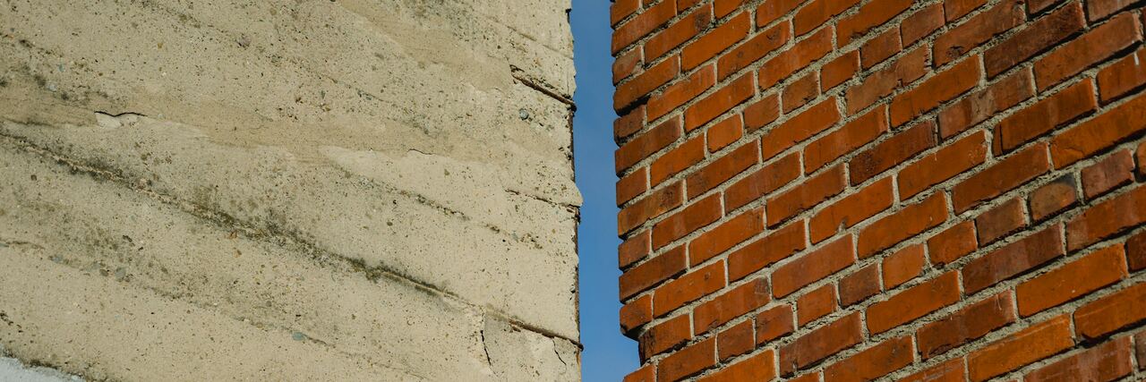 Een muur in beton en een muur in rode baksteen naast elkaar, met een smalle strook blauwe lucht ertussen.