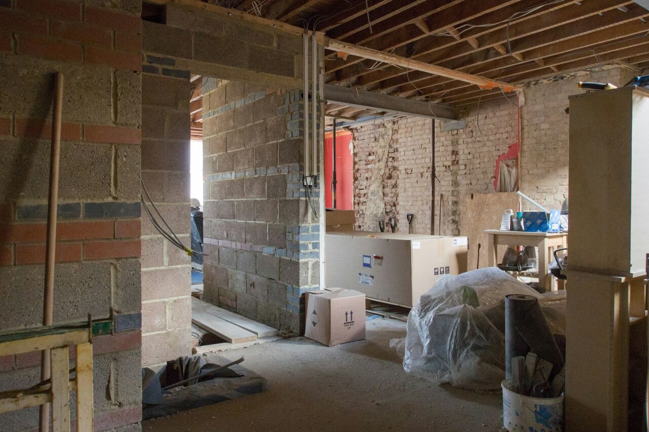 Woning tijdens een renovatie: muren in snelbouwsteen, open plafond met balken en materiaal op de vloer.