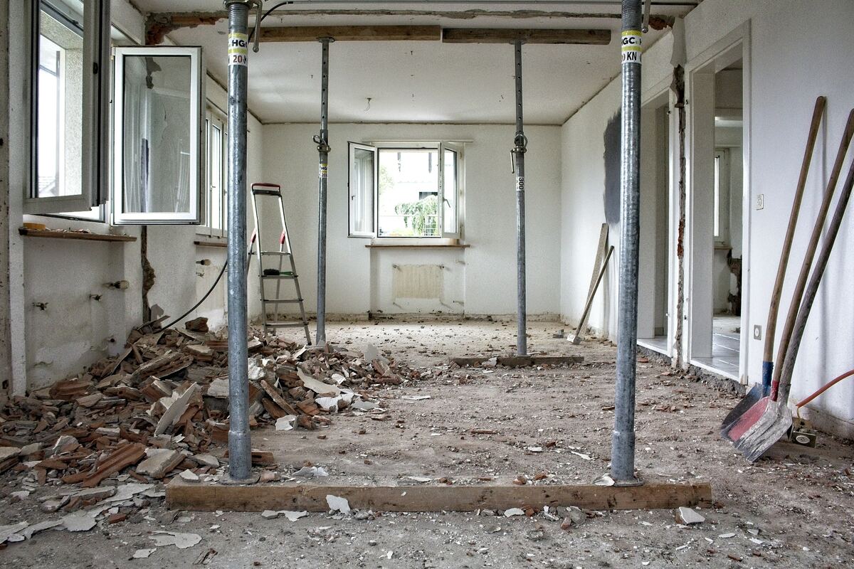 Ruimte in verbouwing met stalen stempels die het plafond ondersteunen, puin op de vloer.