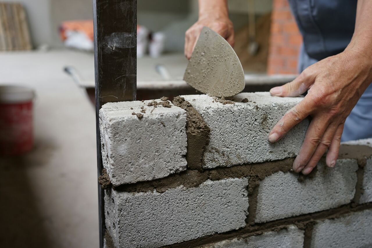 Metselaar legt een betonblok in de mortel, met een troffel in de hand.