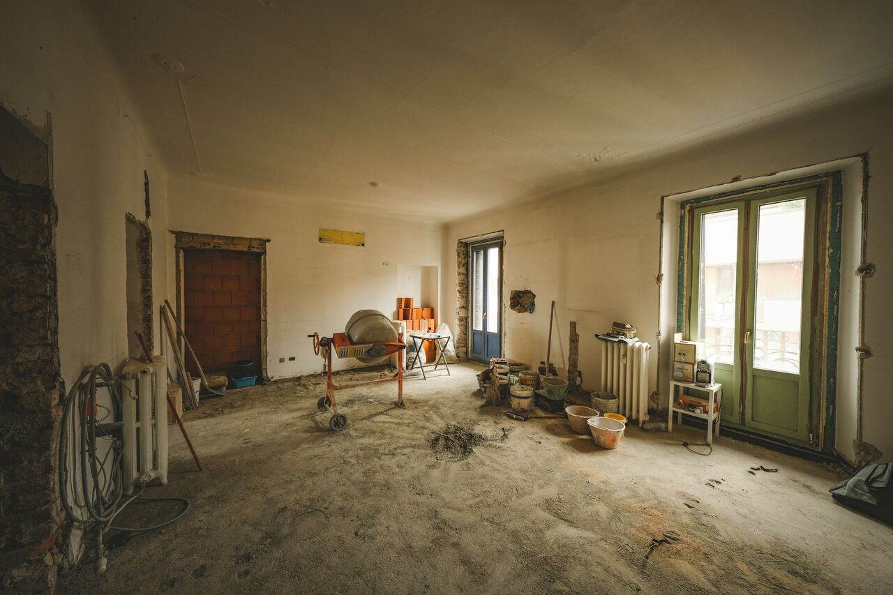 Ruimte in een oudere woning tijdens de renovatie: kale vloer, een betonmolen, radiatoren en openslaande deuren.